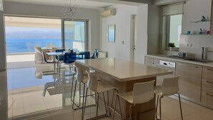 A modern kitchen with a large island, bar stools, and a view of the sea.