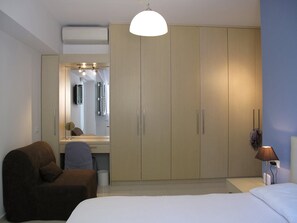 A bedroom with a bed, a brown armchair, a wardrobe, a desk with a mirror, and a hanging lamp. - Luxurious Suite Athena Near To Beach (Malevizi)