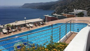 A rooftop pool with clear blue water, lounge chairs, and a view of the sea and mountains.