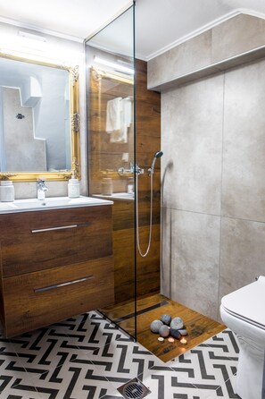 A modern bathroom with a wooden vanity, a glass shower enclosure, and a patterned floor.