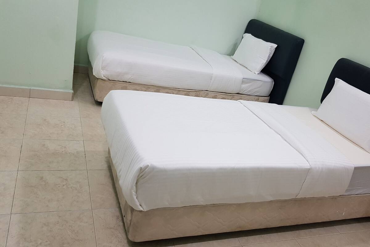 Two single beds with white bedding in a room with light green walls and tiled flooring.