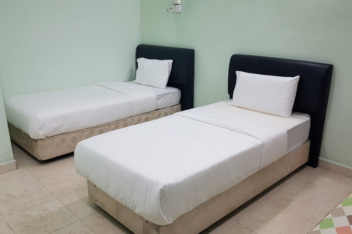 Two single beds with white linens in a room with light green walls and a tiled floor.