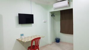 A small room with a television mounted on the wall, a table with a checkered tablecloth, a red chair, a blue trash bin, and a brown curtain. - OYO 89998 thank Q inn 2 (Kota Bharu)