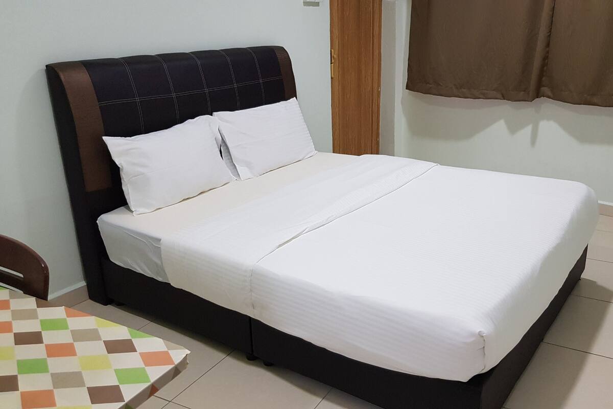 A neatly made bed with white linens in a room with a tiled floor and a brown curtain.