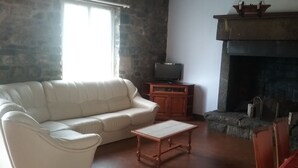 A living room with a white sofa, a wooden coffee table, a television on a wooden cabinet, and a stone fireplace. - old farmhouse of the manor (siouville hague)