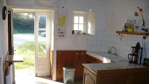 A kitchen with a gas stove, a sink, a window, and a door leading outside. - old farmhouse of the manor (siouville hague)