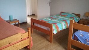 A room with two wooden beds, a small table with a blue object, and a door leading to another room. - old farmhouse of the manor (siouville hague)