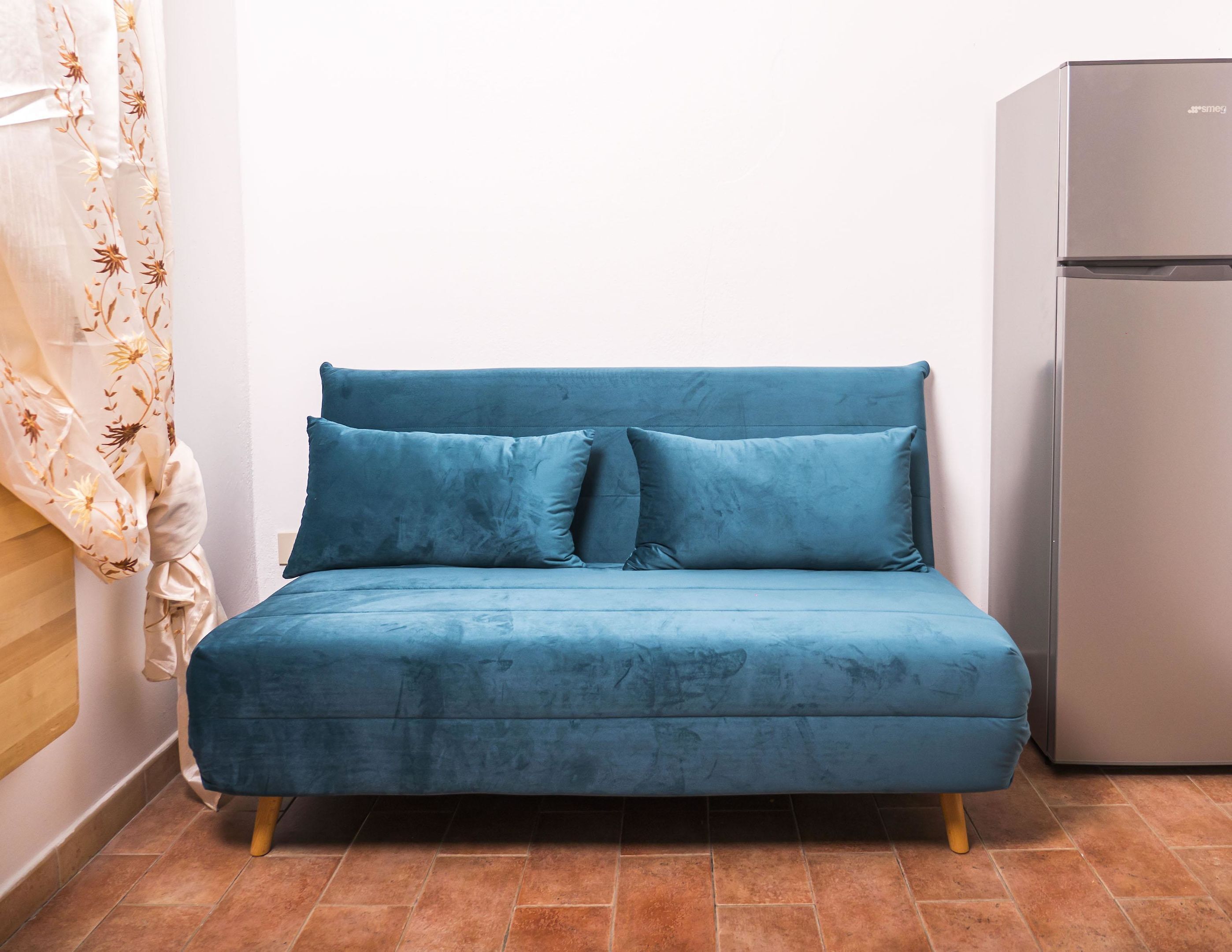 Ein blaues Sofa mit Holzbeinen in einem Raum mit Fliesenboden und einem Kühlschrank.