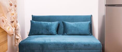 Ein blaues Sofa mit Holzbeinen in einem Raum mit Fliesenboden und einem Kühlschrank.