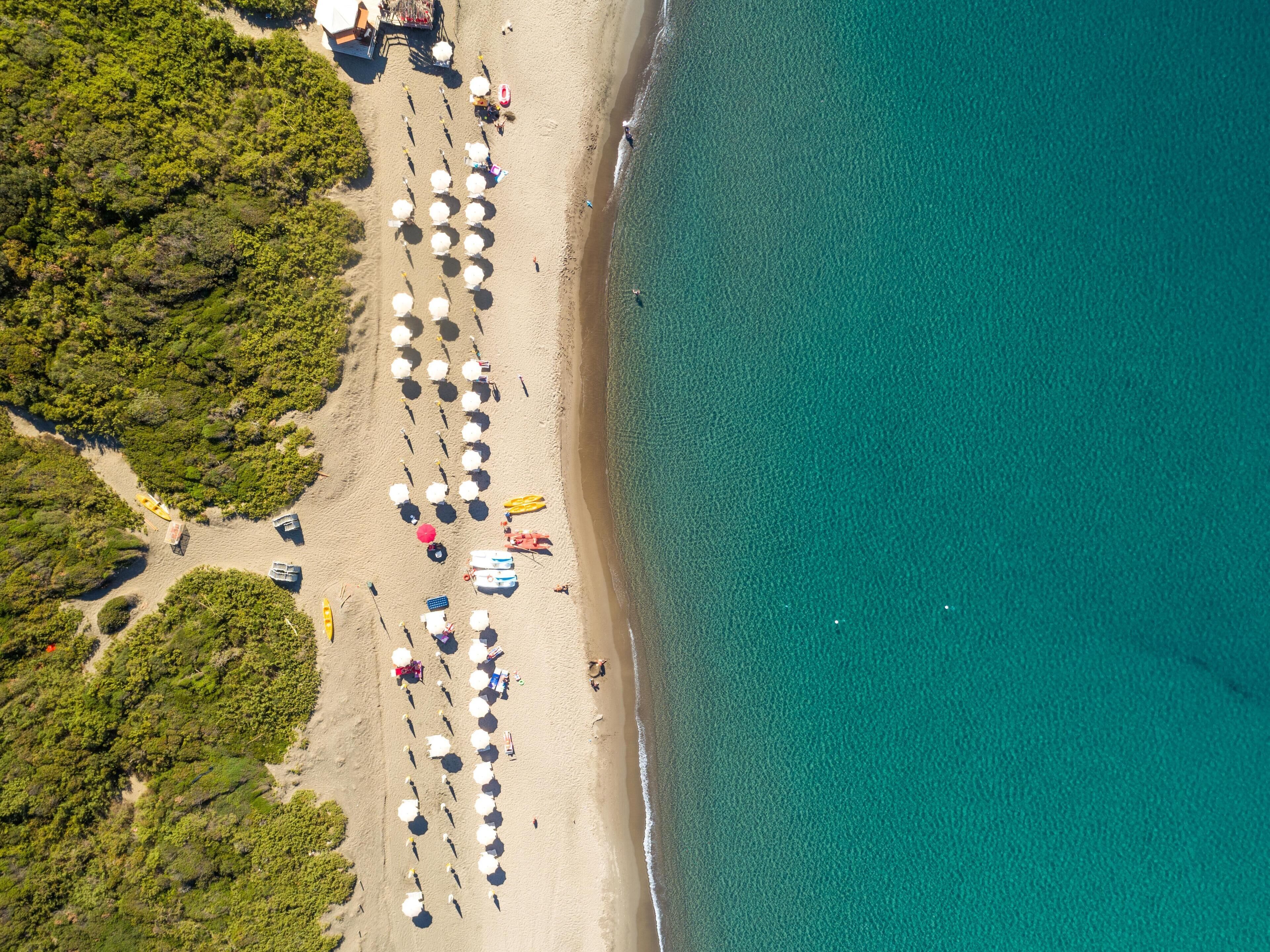 Een privéstrand, zwart zand, ligstoelen aan het strand, parasols