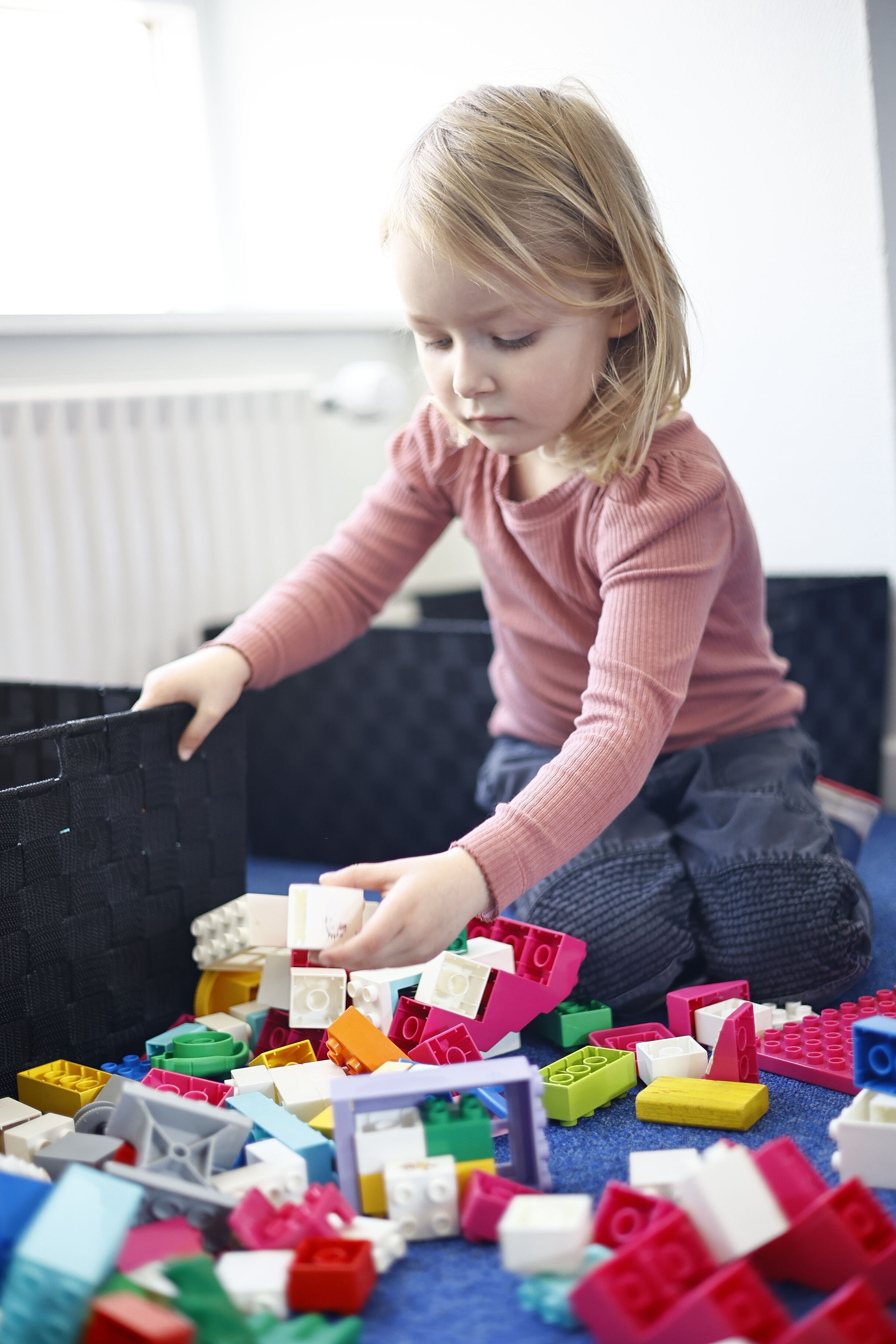 Een kind speelt met kleurrijke blokken op een blauw tapijt.