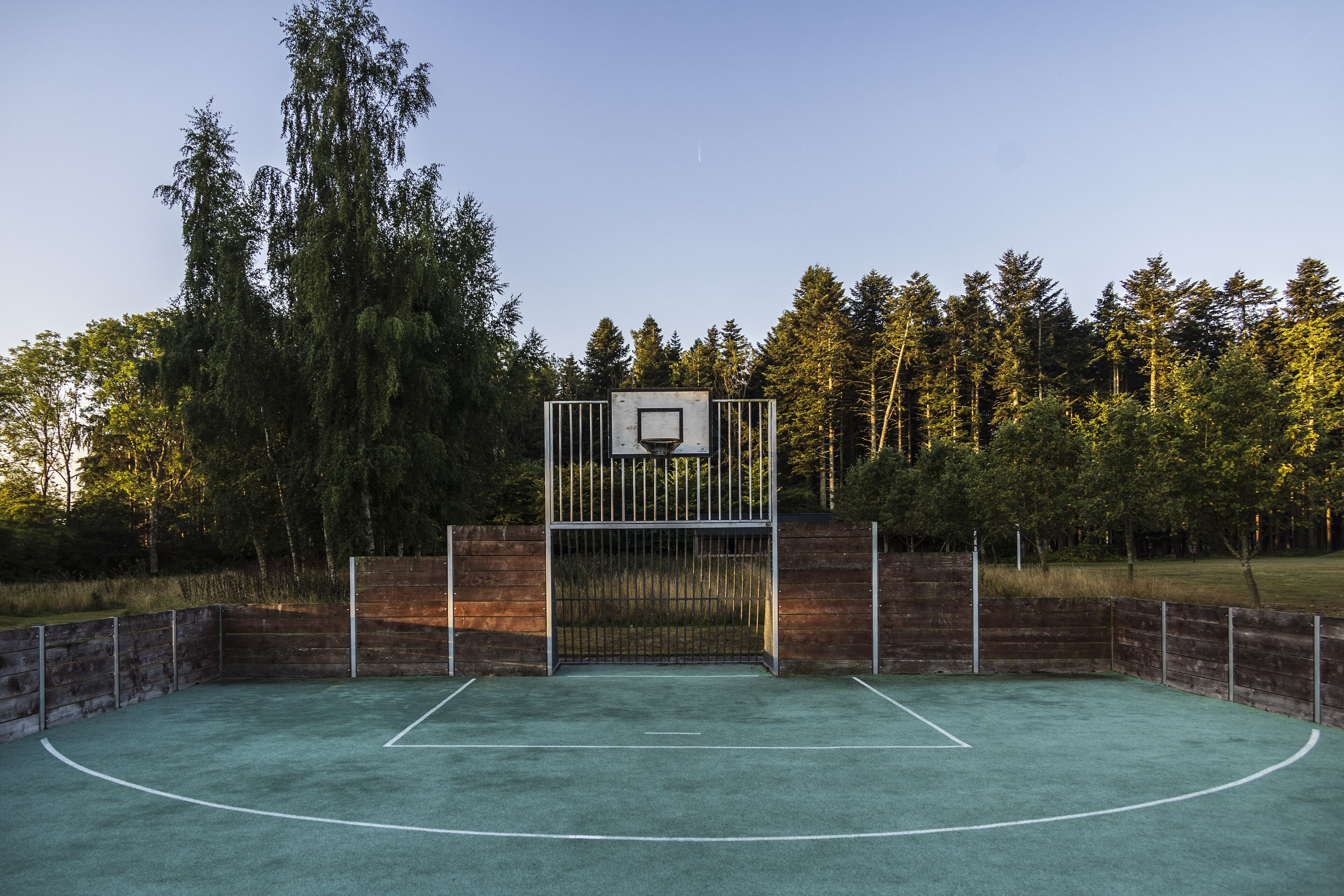 An outdoor basketball court with a metal gate and a basketball hoop.