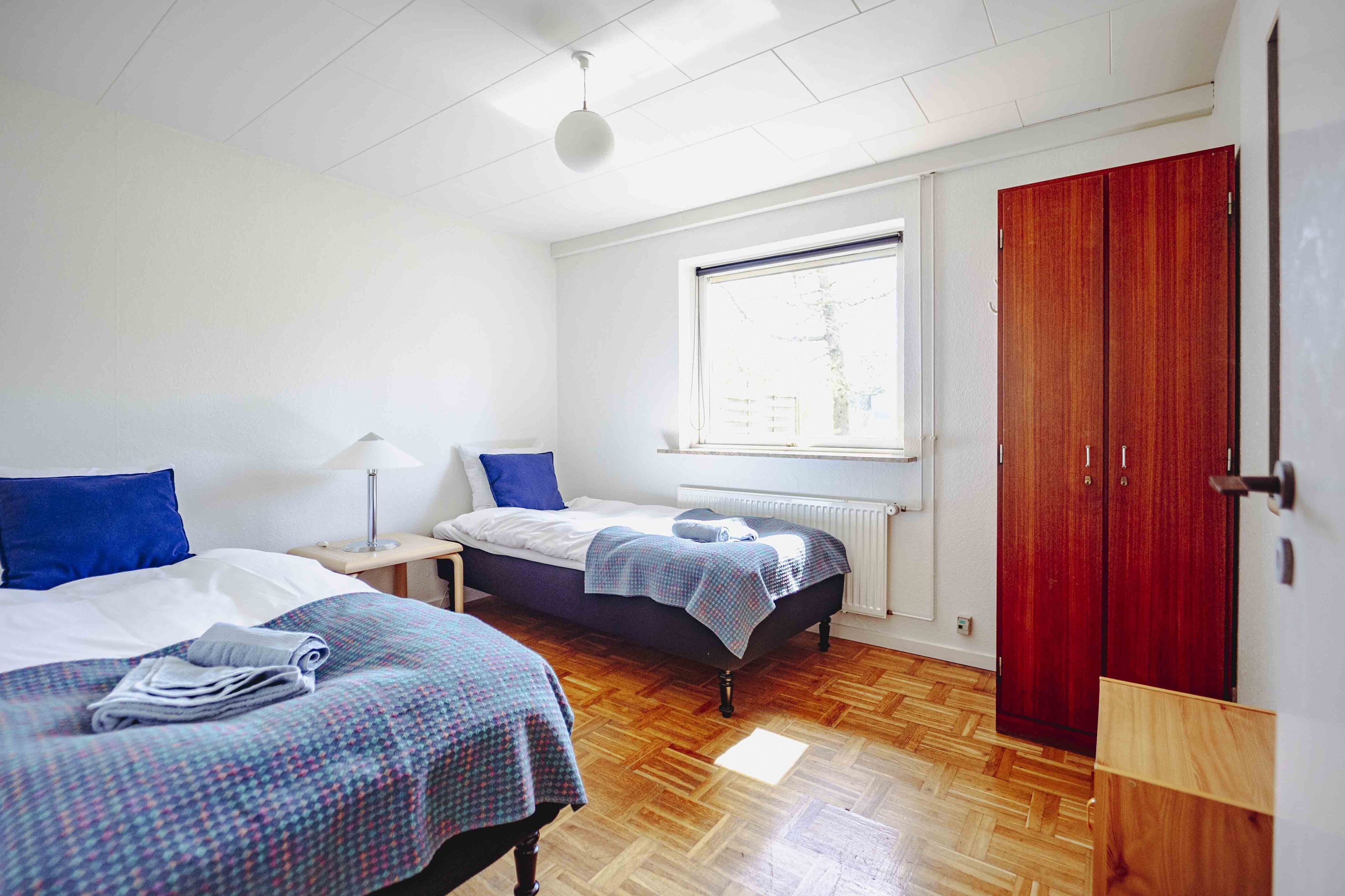 A bedroom with two beds, a window, a radiator, and a wardrobe.