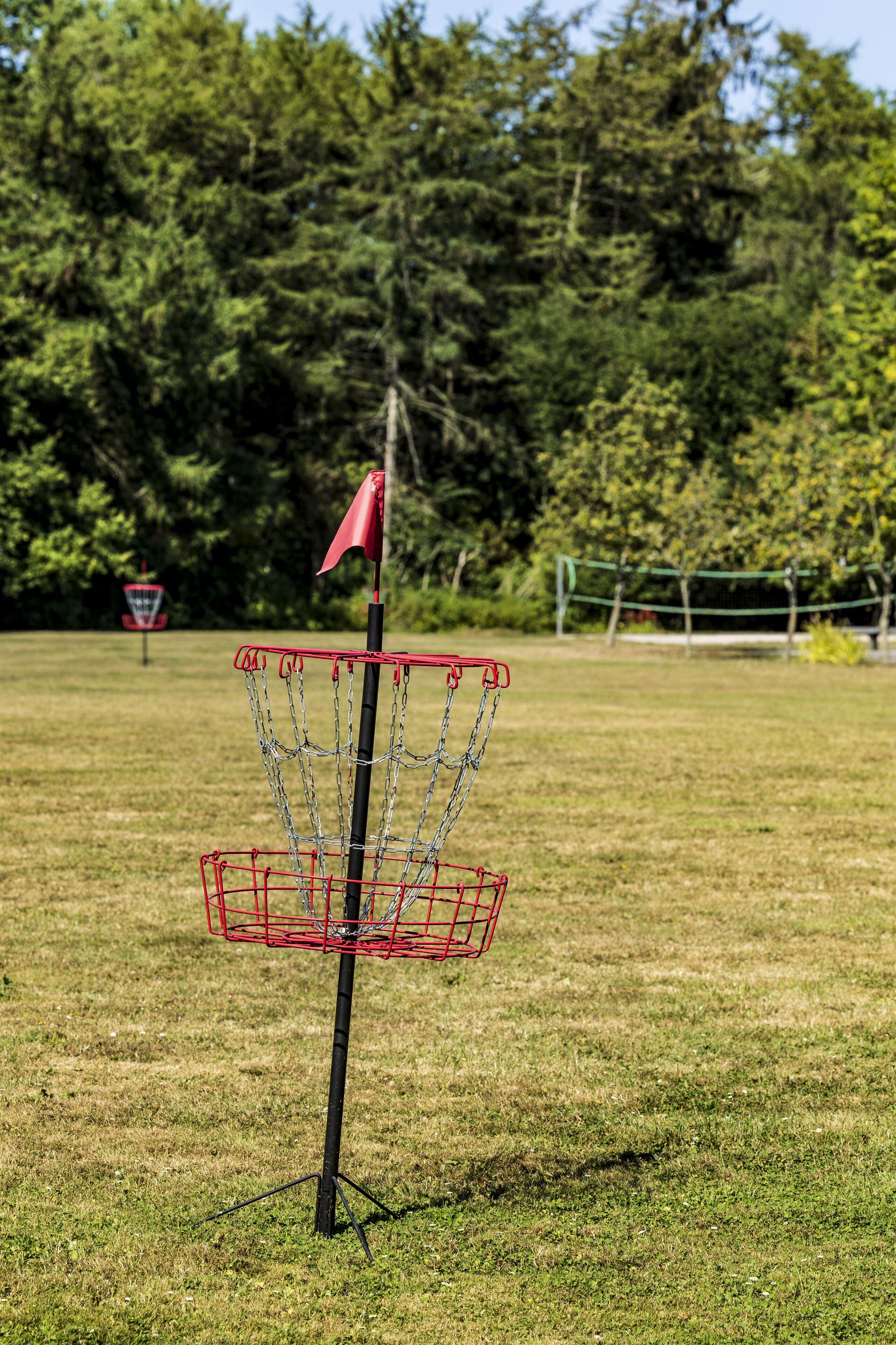 A disc golf basket with a red flag on a grassy field.