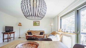 A modern living room with a wooden dining table, a sofa, and a television on a wooden stand. - Pederstrup Bed and Breakfast (Torrig)
