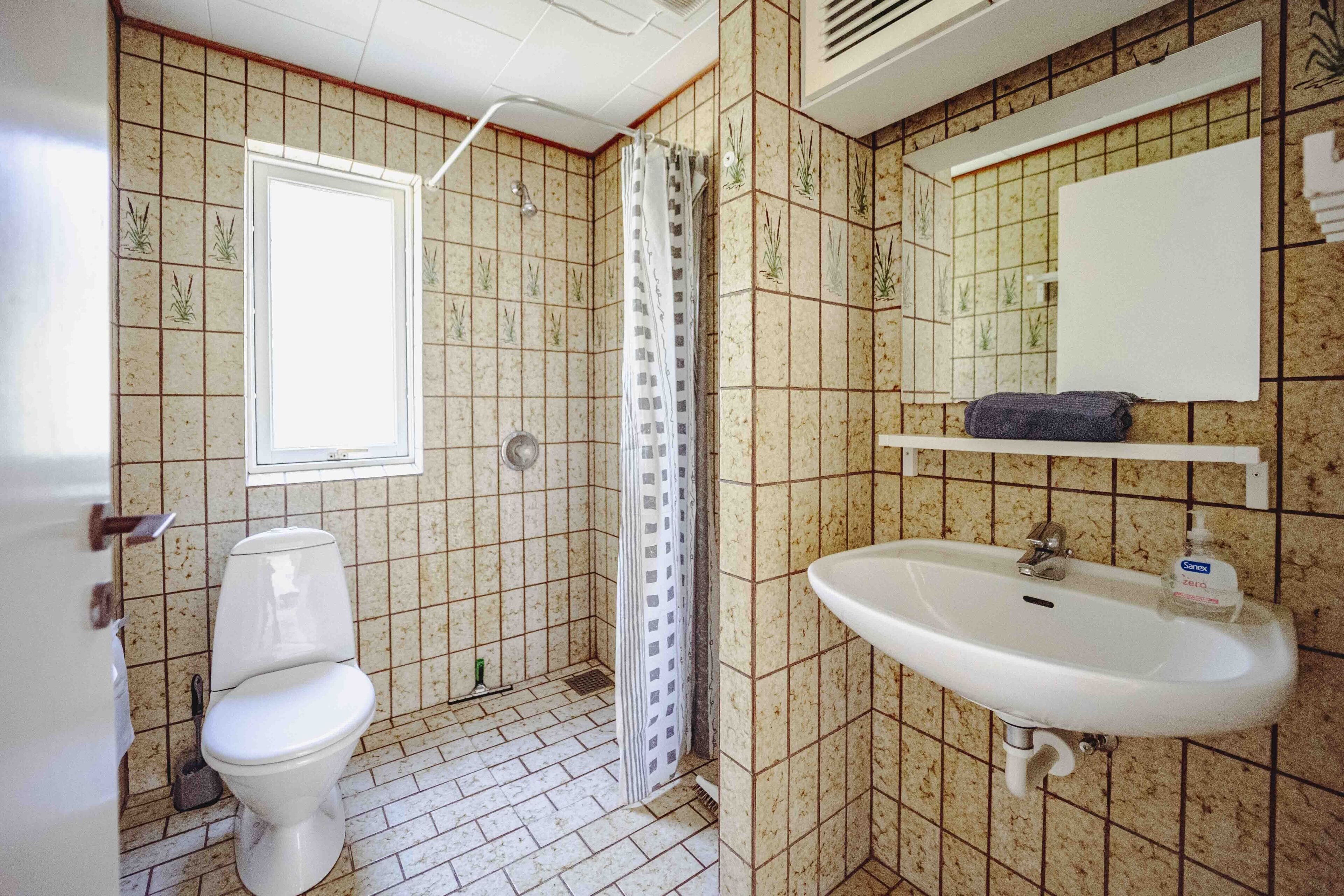 A bathroom with a toilet, shower, sink, and a window.