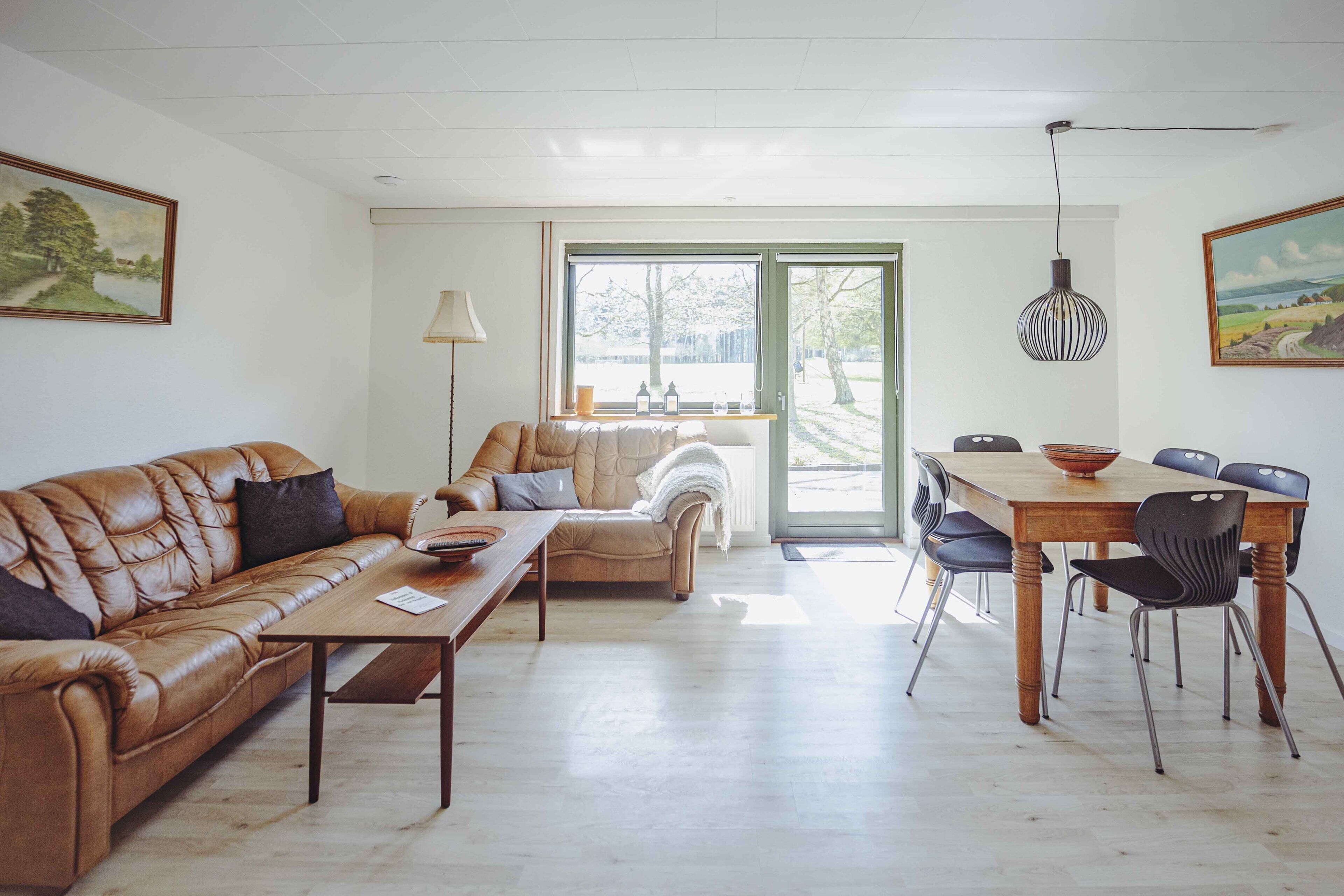 Un salon spacieux avec un canapé en cuir, une table basse en bois et un coin repas comprenant une table et des chaises en bois.