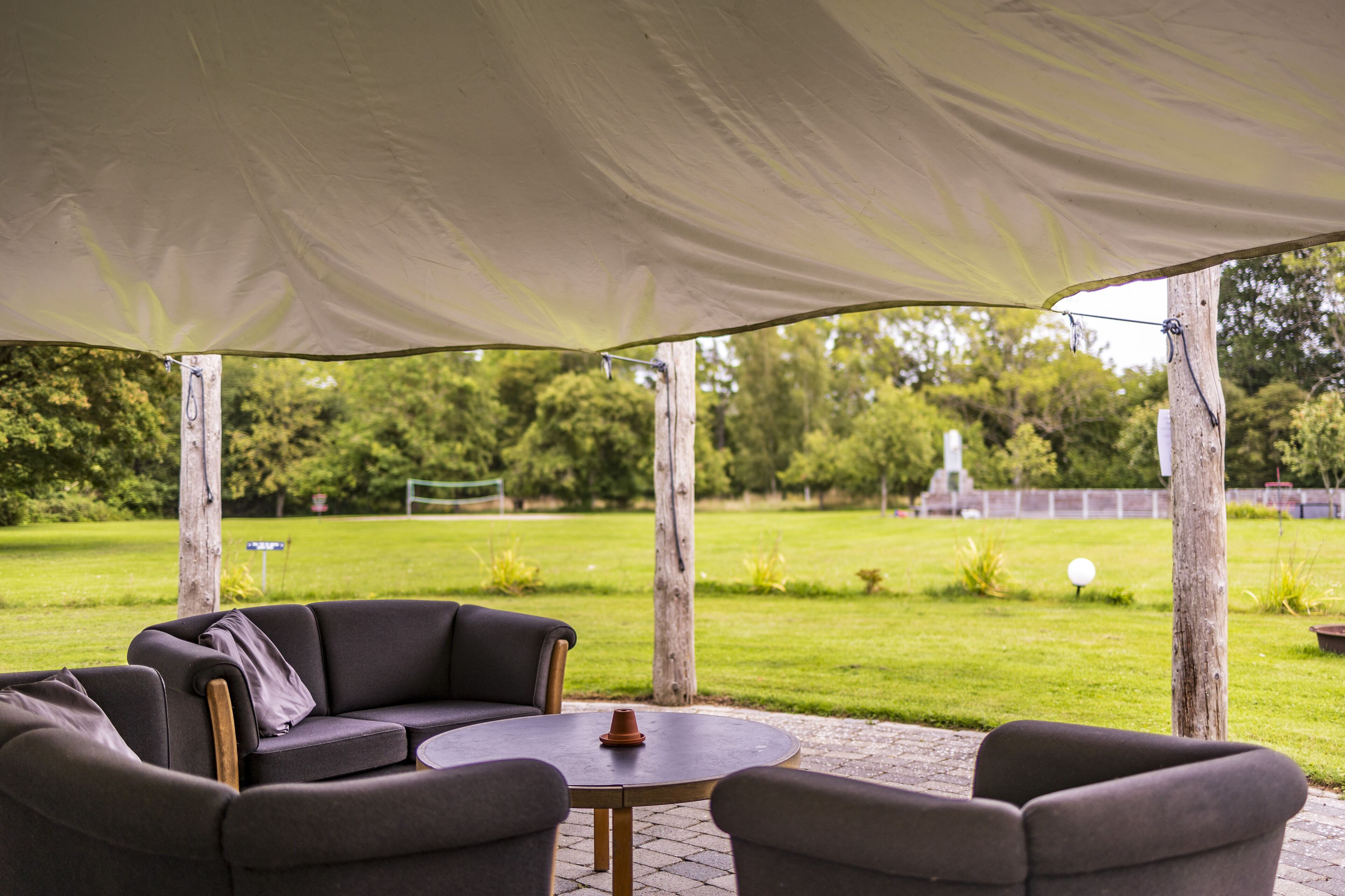 Une terrasse extérieure dotée d’un espace salon couvert, comprenant un canapé et deux fauteuils, ainsi qu’une petite table ronde.