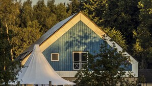 A blue building with a white roof, surrounded by trees and a grassy area with a white tent and some outdoor furniture. - Pederstrup Bed and Breakfast (Torrig)