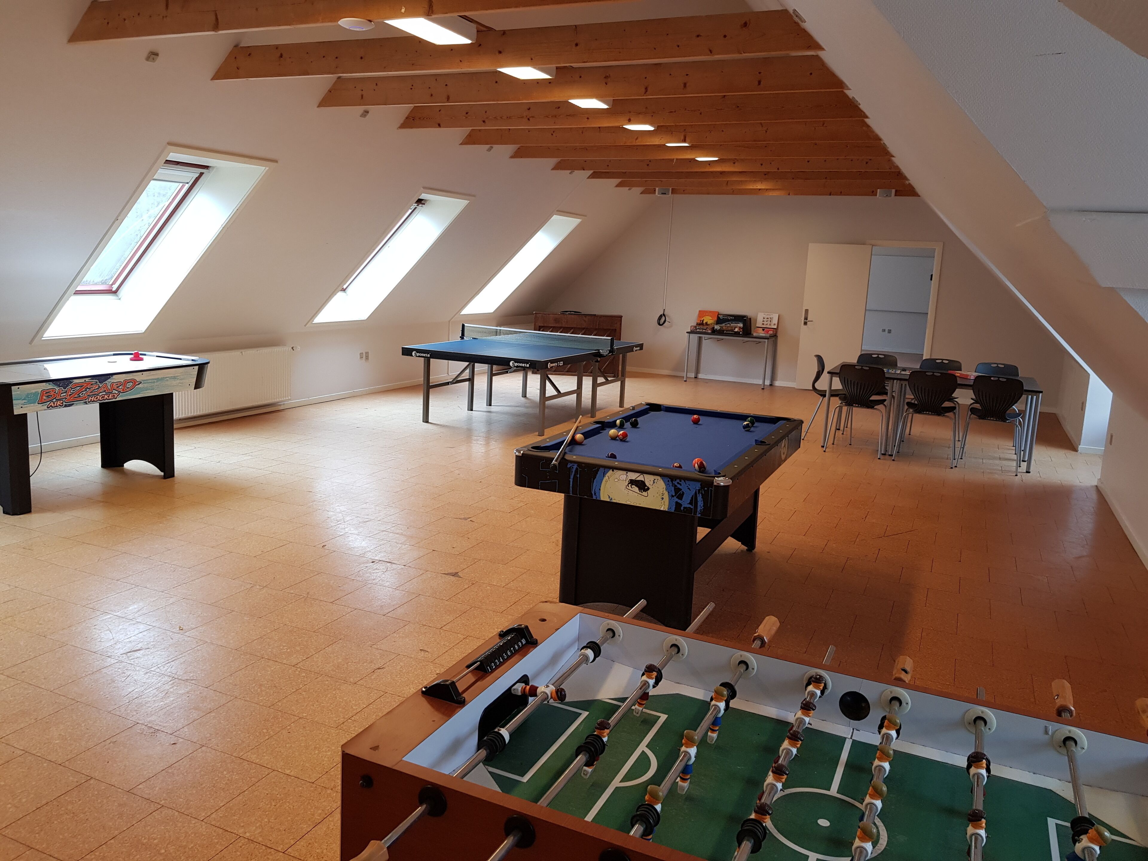 Een ruime kamer met een tafelvoetbaltafel, een pingpongtafel en een pooltafel.