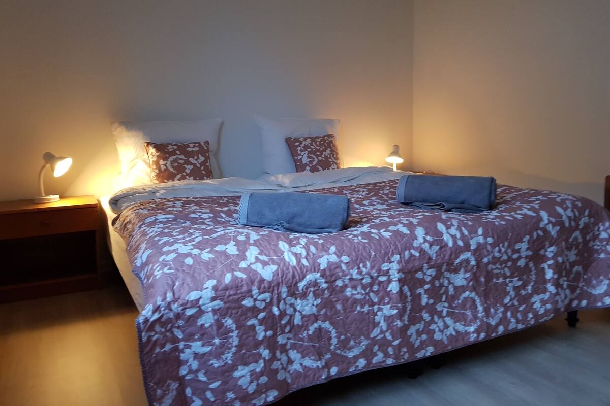 A neatly made bed with a floral-patterned bedspread and two pillows, flanked by bedside tables with lamps.