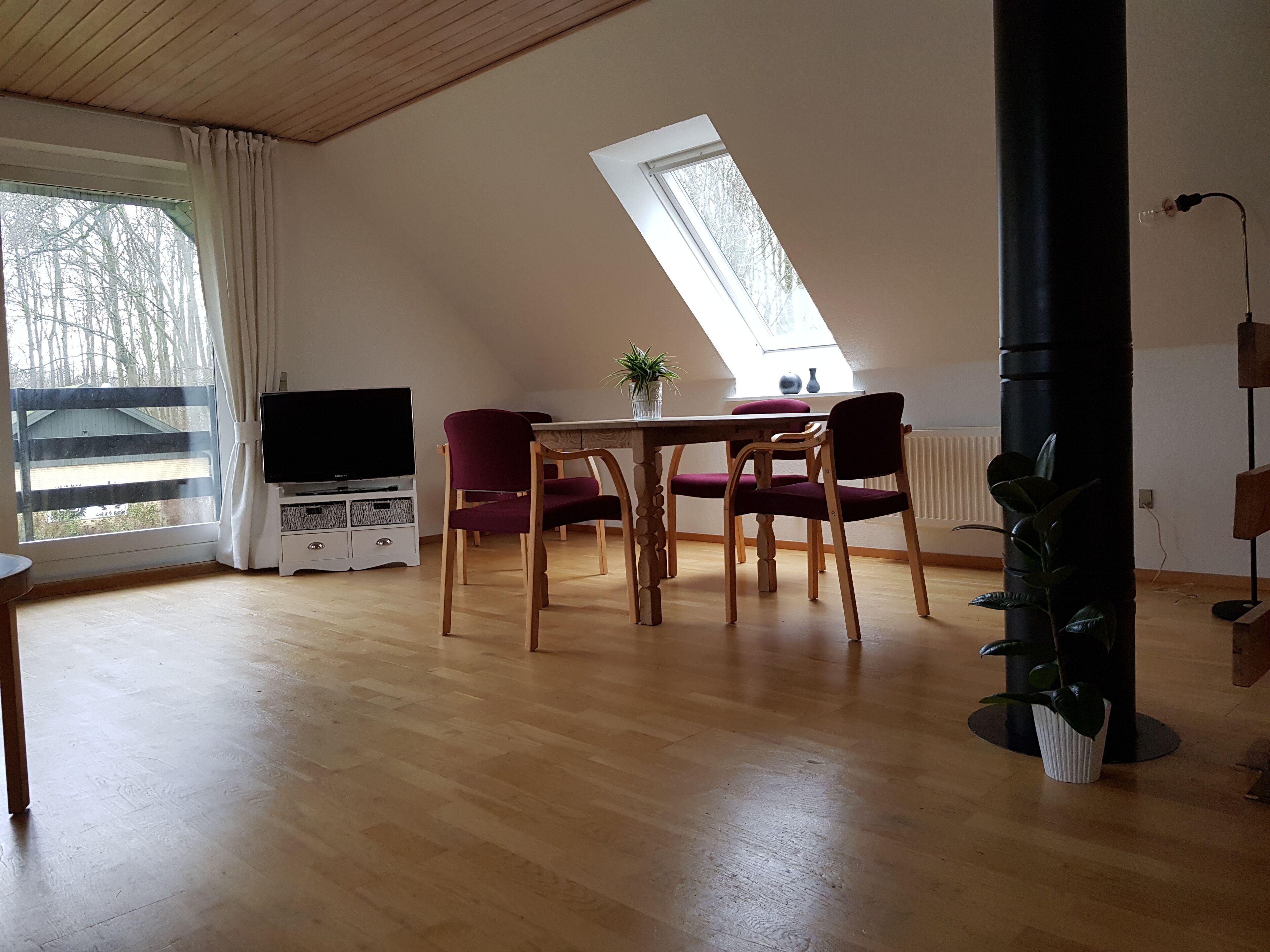 A spacious room with a wooden floor, a dining table with chairs, a TV, and a skylight.
