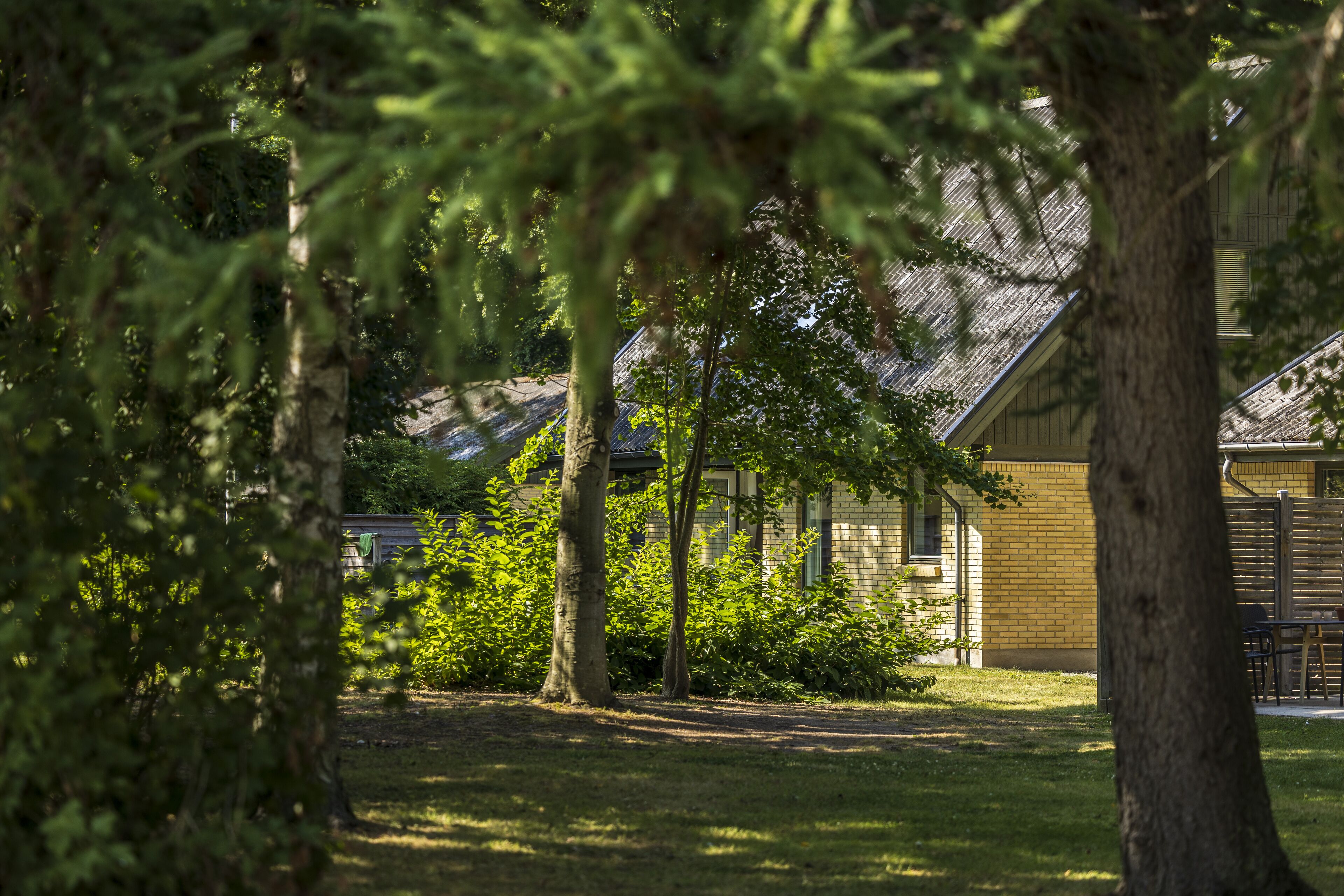 A building with a brick exterior and a sloped roof, surrounded by trees and a grassy area.