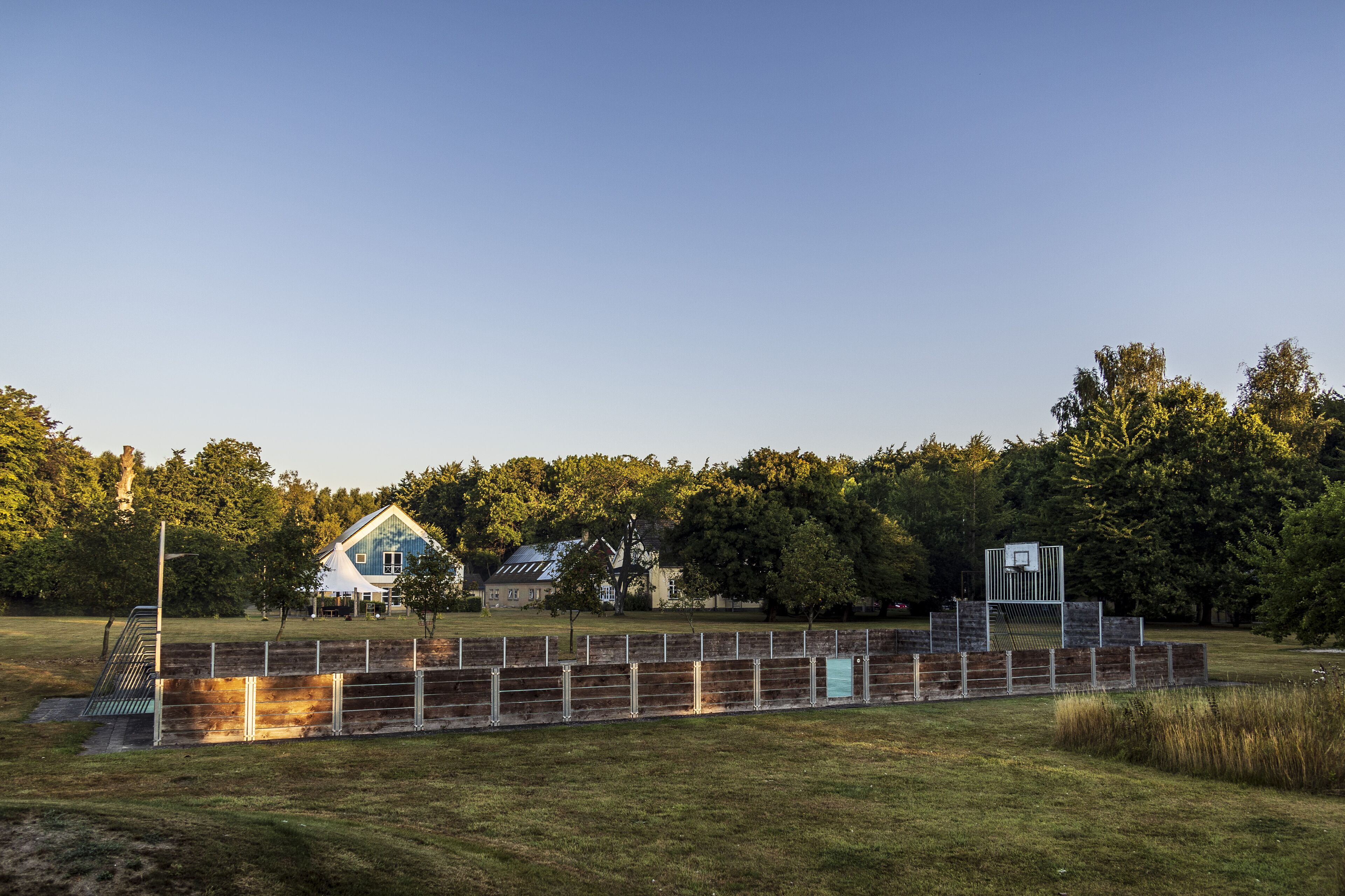 Un terrain de sport clôturé avec un terrain de basket et une maison en arrière-plan.