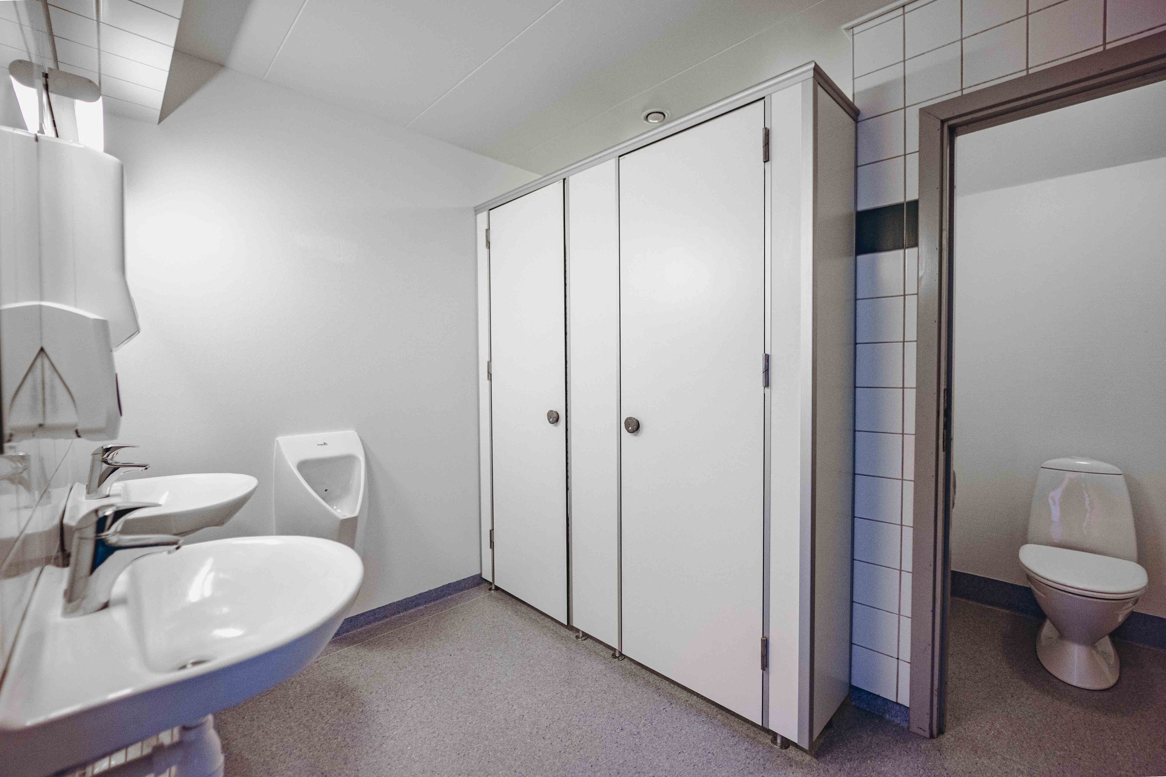 A bathroom with a sink, mirror, urinal, toilet, and a wardrobe.