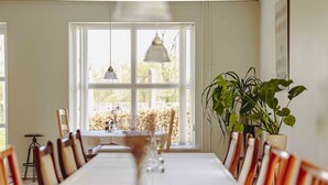 A dining room with a long table, chairs, a potted plant, and a window with a view of trees. - Pederstrup Bed and Breakfast (Torrig)