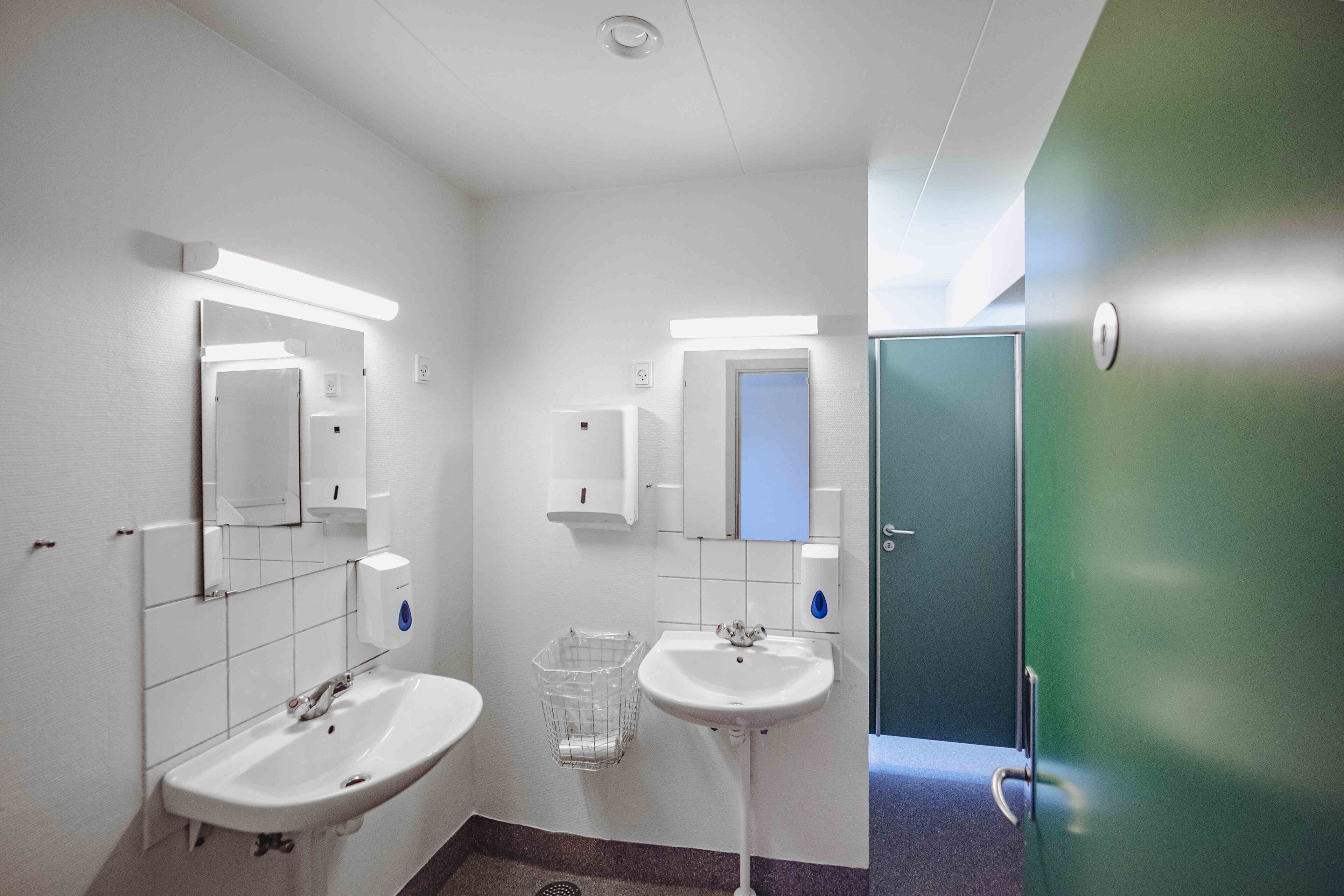 Een schone, moderne badkamer met twee wastafels, een spiegel en een prullenbak.