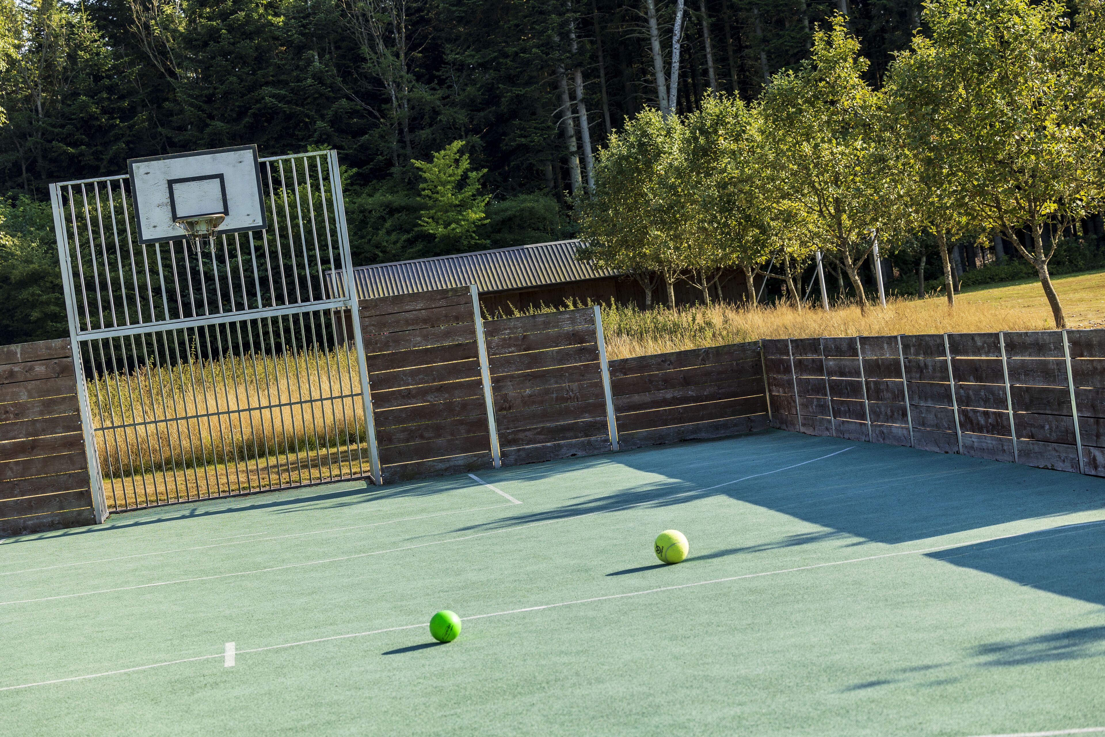An outdoor tennis court with a metal fence and trees in the background.