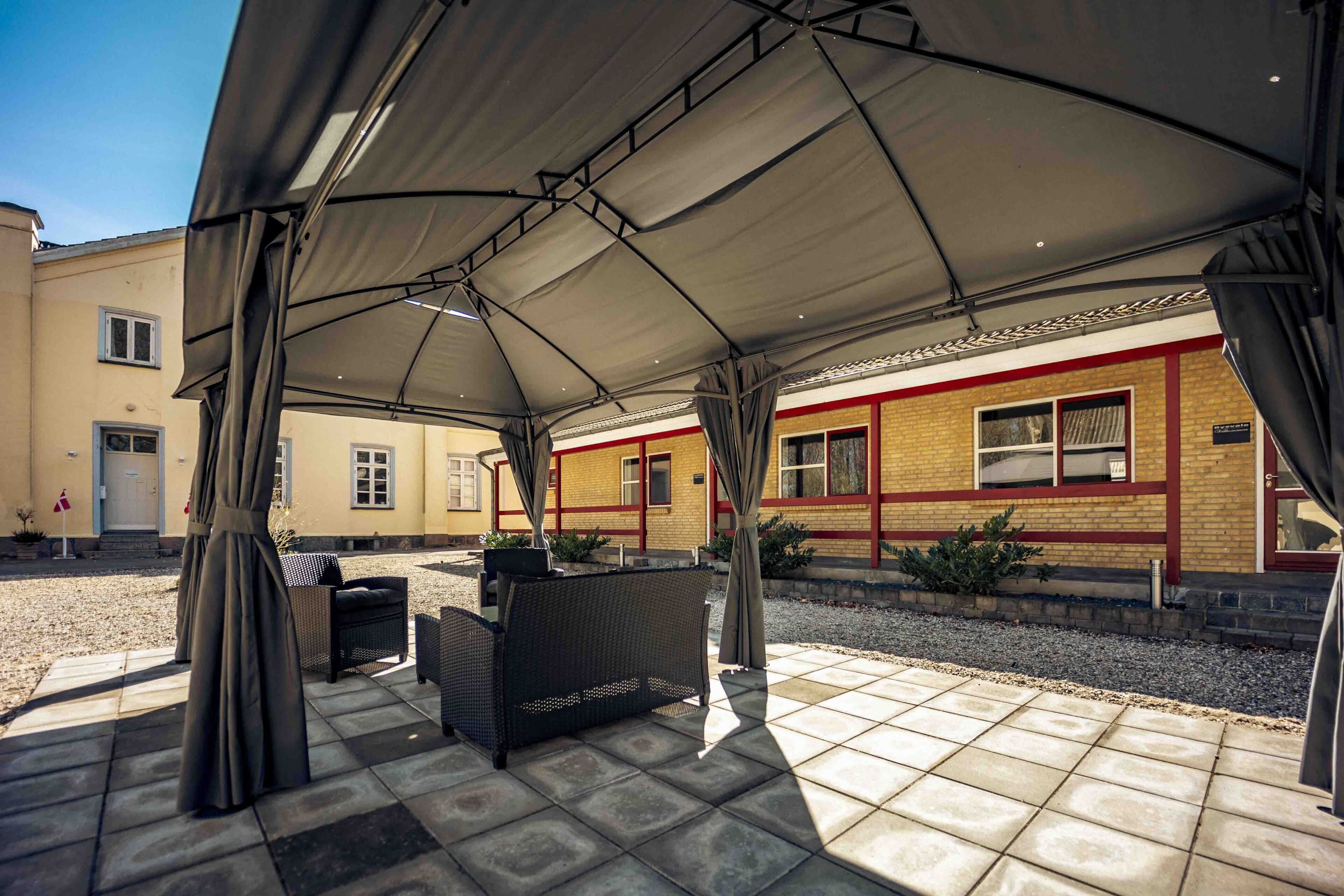 An outdoor covered patio area with wicker furniture and a tiled floor.