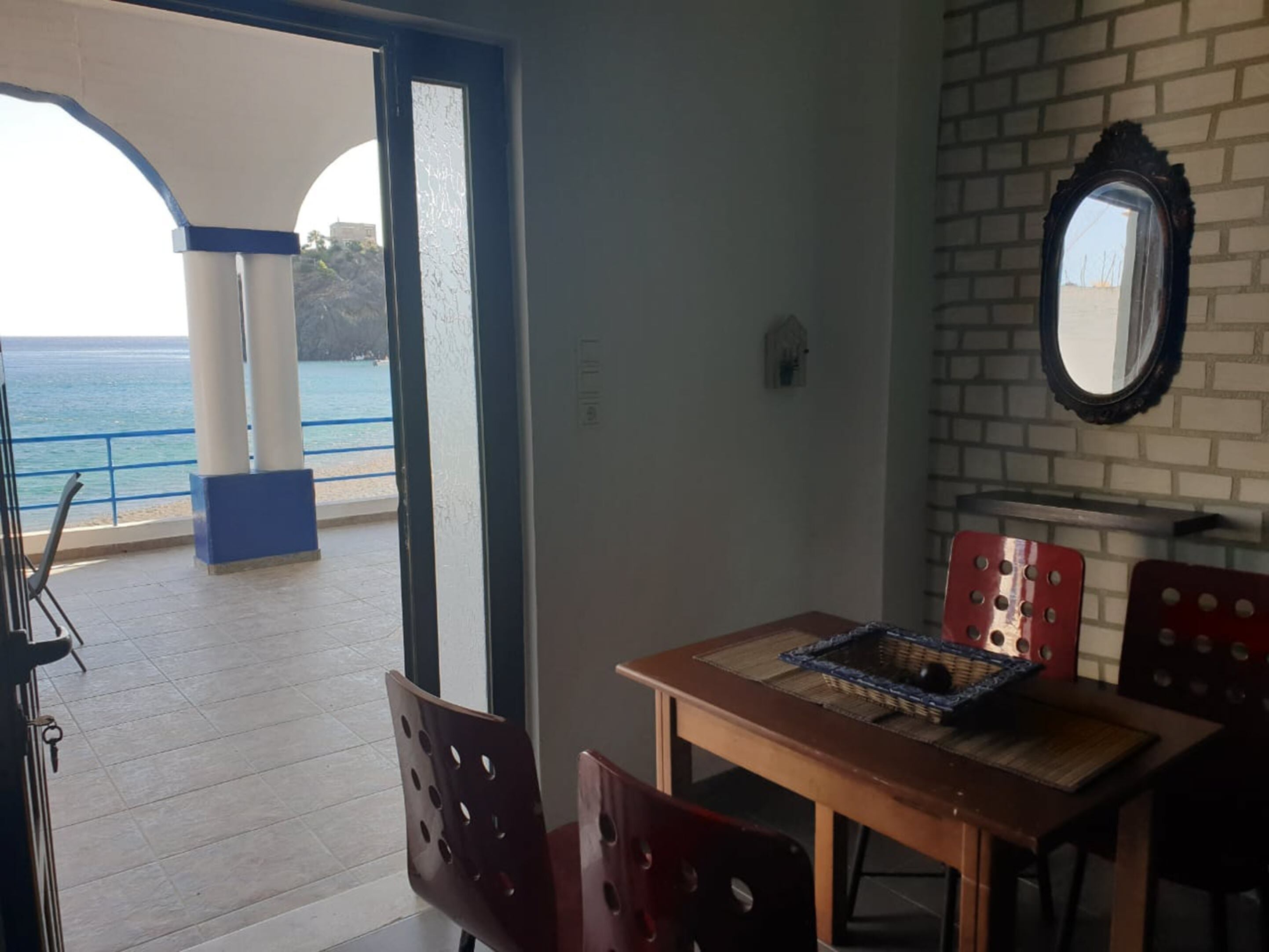 A room with a view of the sea, a wooden table with chairs, a mirror on the wall, and a small decorative item on the table.