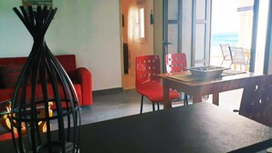 A room with a red sofa, a dining table with chairs, and a view of the sea through a large window.