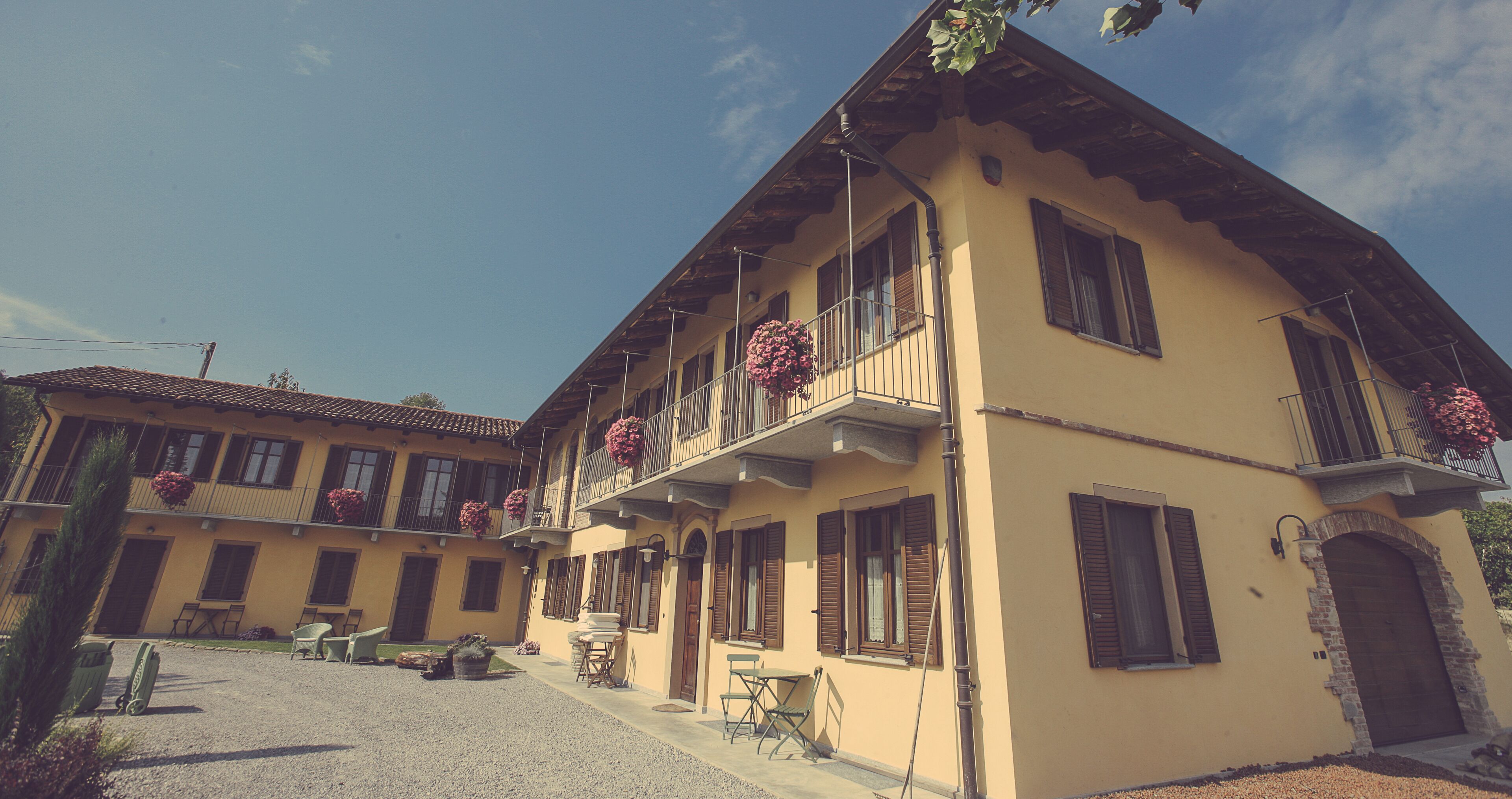 A yellow building with multiple balconies, outdoor seating, and a gravel driveway.