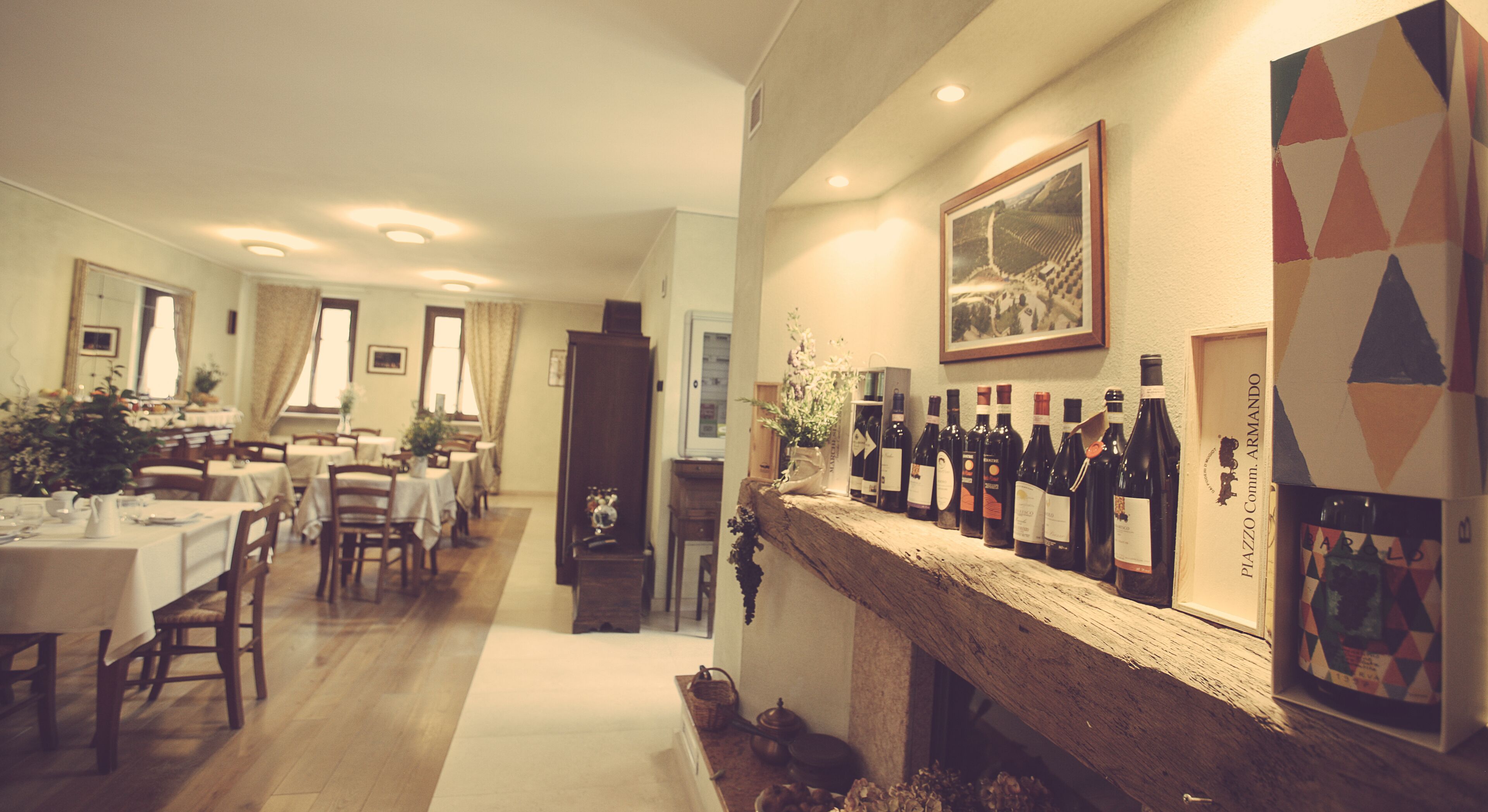 Un área de comedor con mesas y sillas, una chimenea con botellas de vino, y una pared con obras de arte enmarcadas.