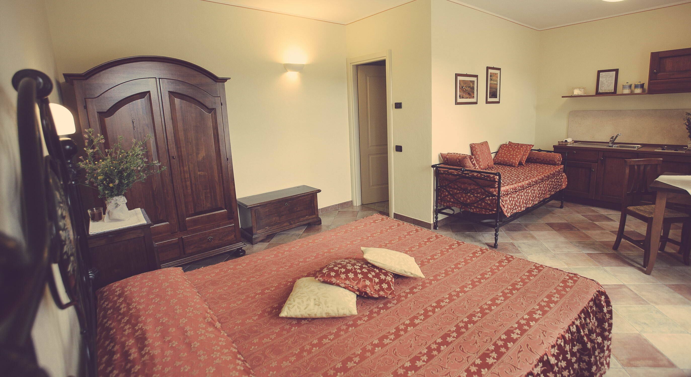 Een slaapkamer met een groot bed, een houten garderobe, een bureau en een kleine keukenhoek.