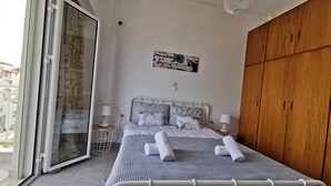 A bedroom with a bed, two bedside tables, a wooden wardrobe, a window, and a wall-mounted artwork. - Andreas Cozy Lovely House (Heraklion)