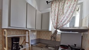 A compact kitchen with white cabinets, a stove, a sink, and a window with floral curtains. - Andreas Cozy Lovely House (Heraklion)