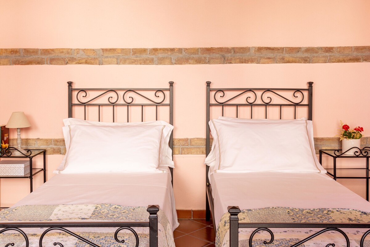 Une chambre double avec deux lits, un mur en briques et une petite table avec une lampe.