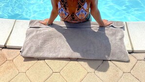 En person sidder på et håndklæde ved en swimmingpool med klart vand.