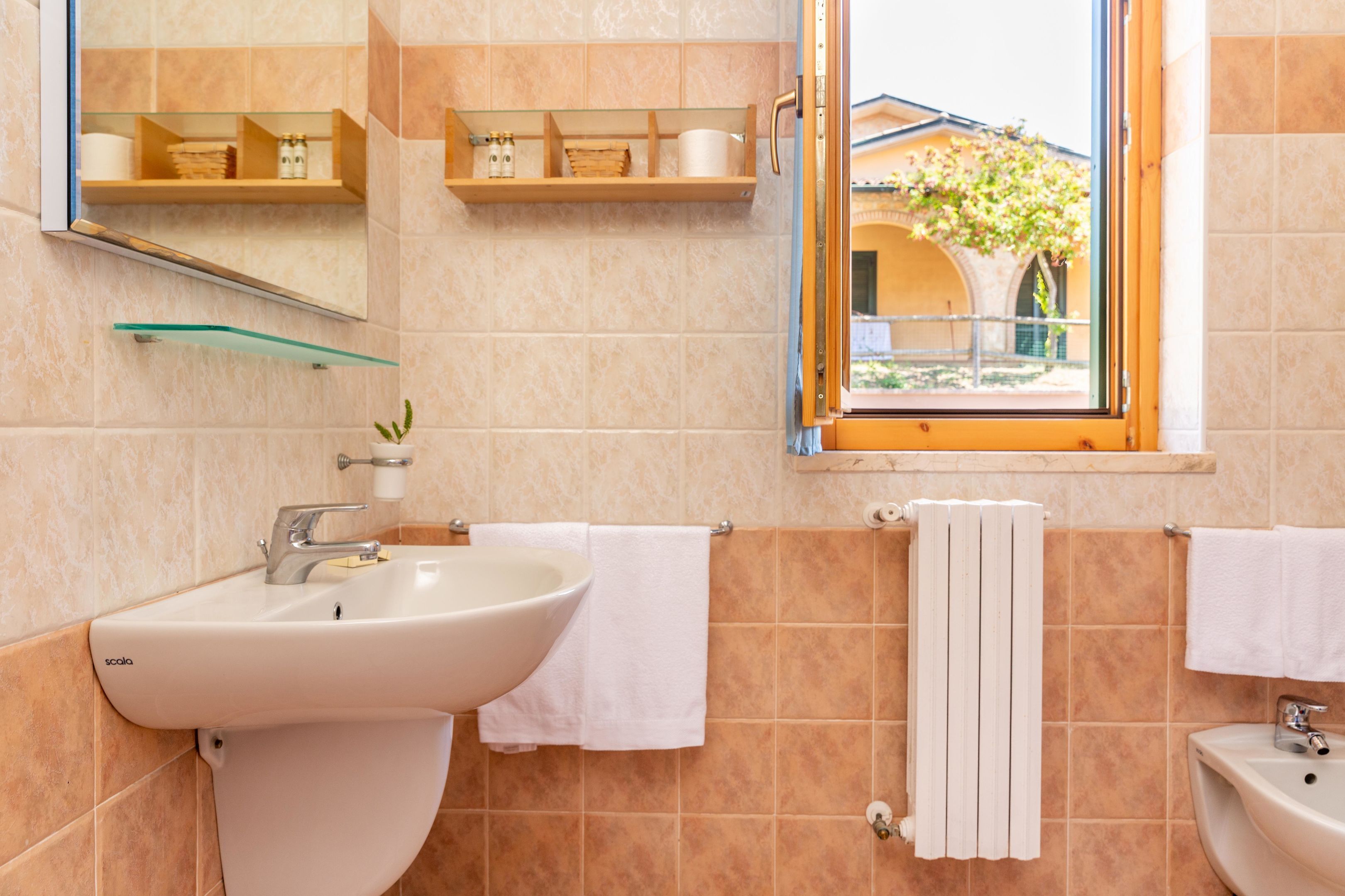 A bathroom with a sink, mirror, towel rack, and a window with a view of a building and tree.