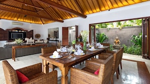 A dining area with a wooden ceiling, wicker furniture, and a view of the garden. - Villa Rubina (Seminyak)