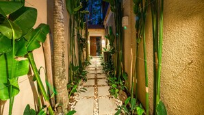 A narrow pathway flanked by lush greenery and a textured wall, leading to a wooden door. - Villa Seacluded 1 (Seminyak)
