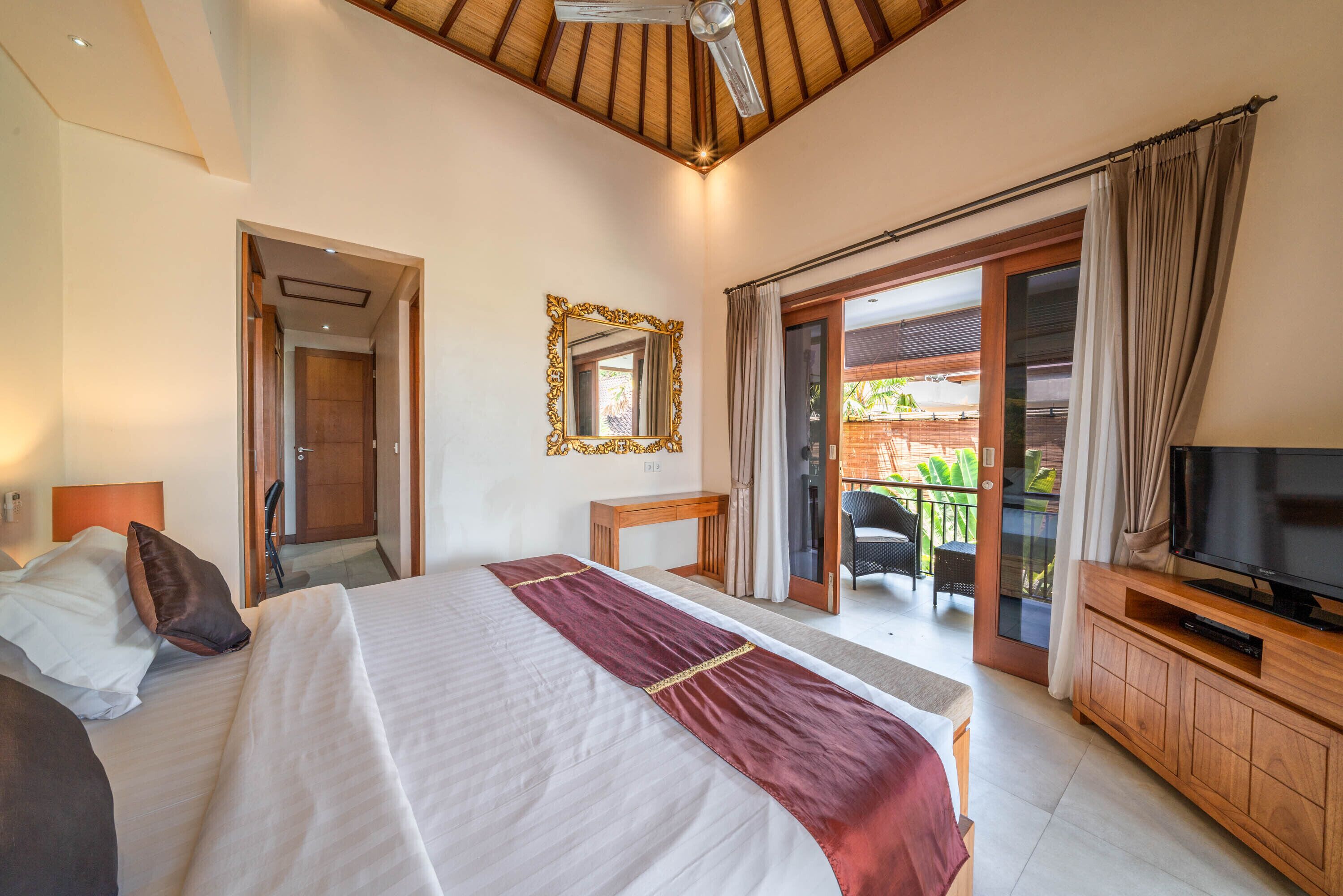A hotel room with a large bed, a television, a wooden cabinet, and a balcony with outdoor furniture.