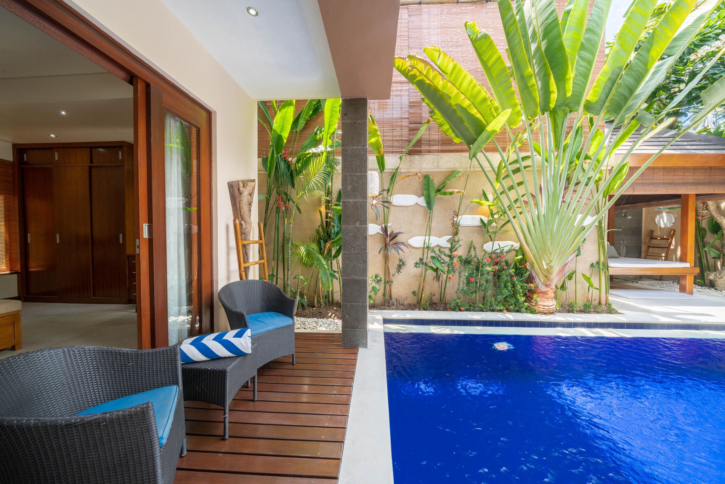 Un espace aménagé au bord de la piscine, avec une terrasse en bois, des meubles en osier et des plantes tropicales.
