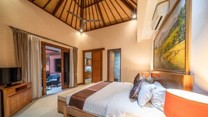 A bedroom with a large bed, a TV, a wooden nightstand, and a painting on the wall. - Villa Seacluded 1 (Seminyak)