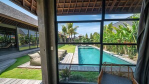 A modern pool area with a clear view through large windows, a wooden deck, and outdoor seating. - Villa Wirtiga (Canggu)