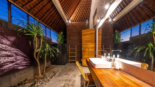 A modern bathroom with a wooden vanity, a large mirror, and a sink. There are plants and a ladder in the background. - Villa Wirtiga (Canggu)